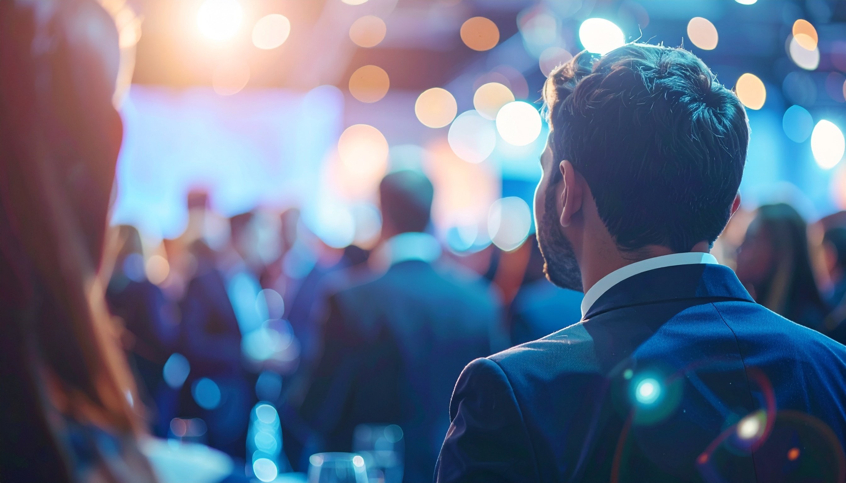 Audience watching a corporate presentation in an auditorium, close up of lady and man's back profile
